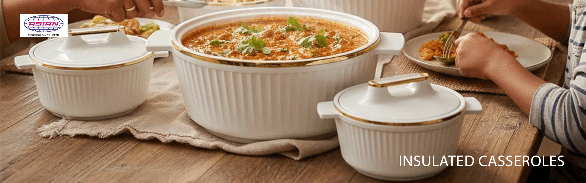 White insulated casseroles with gold trim on a wooden table, people eating around them.