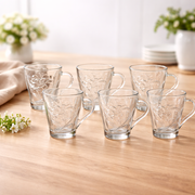 Set of clear glass mugs on a wooden table with flowers in the background