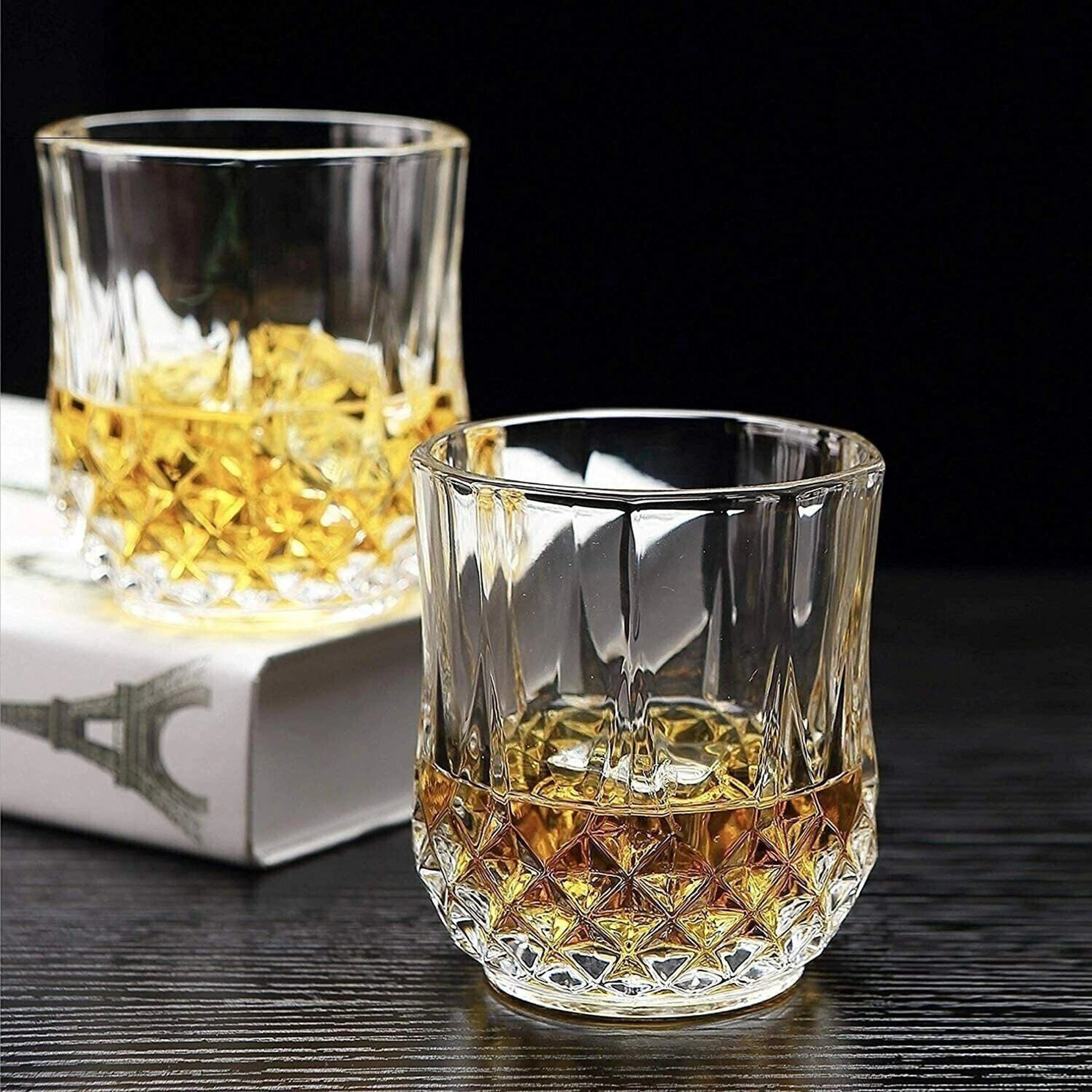 Two crystal glasses filled with whiskey on a dark surface.
